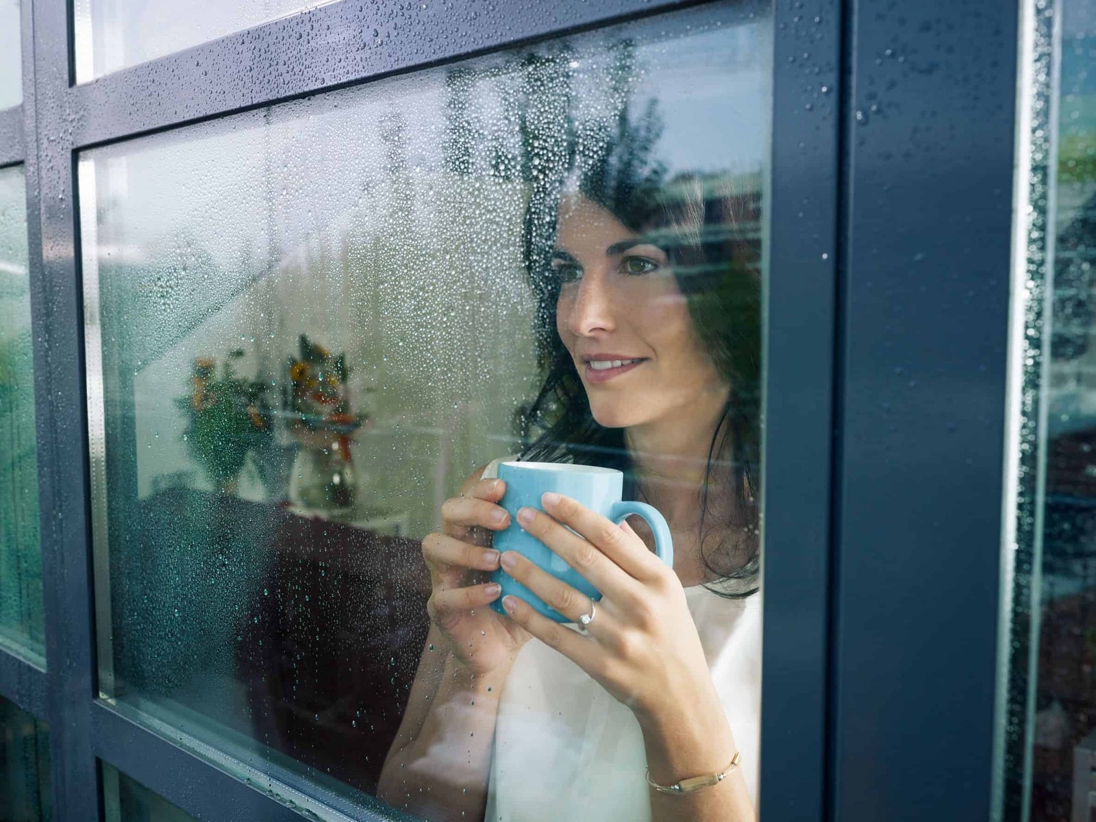 Woman standing looking out a window with a cup in her hands