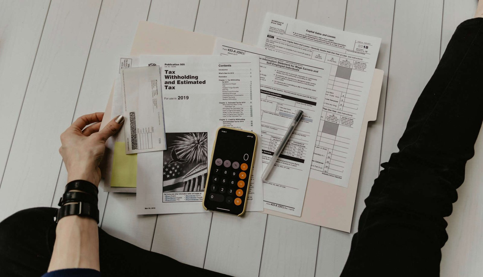 Person seated on floor with tax return forms, a calculator and a pen