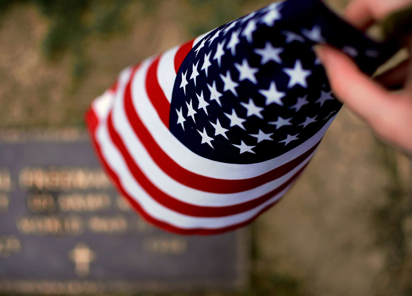 Person folding a small American Flag with a gravestone in the background