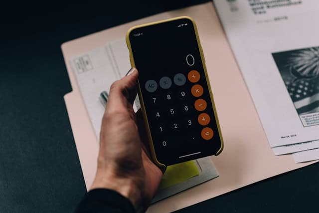 Hand holding smartphone calculator over an open file with papers