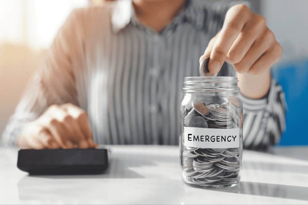 Person putting coins into a jar labelled emergency