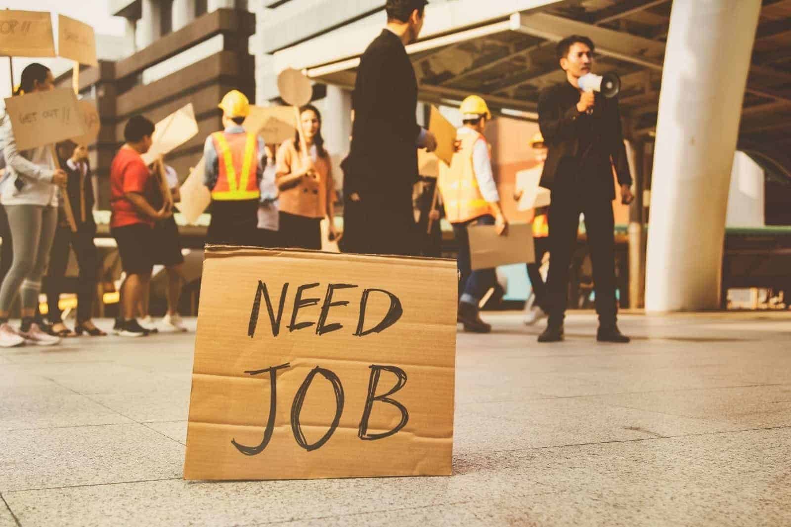 A need job sign on the floor with demonstrating workers in the background