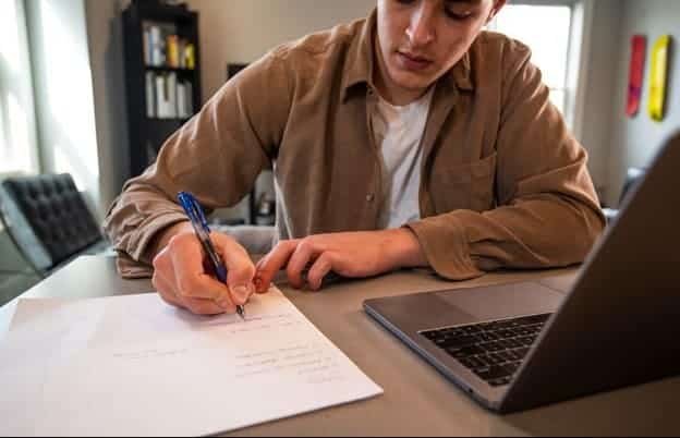 Man seated at a desk in front of a laptop writing down on a piece of paper