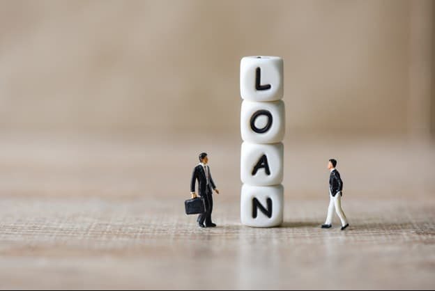 two male figurines walking towards stacked blocks that spell loan 