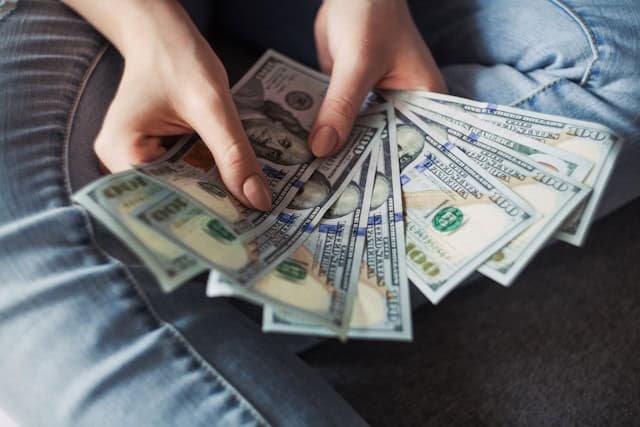 Lady seated on floor with hundred-dollar bills spread in her hands 